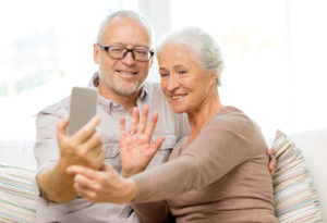 33043006 - family, technology, age, gesture and people concept - happy senior couple with smartphone making selfie and waving hand at home